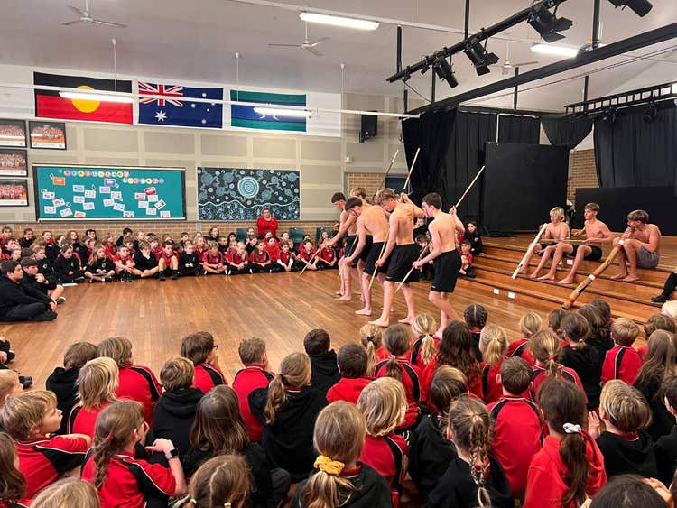 Students sit on the floor in our school hall and watch high school students with spears perform an Aboriginal dance.