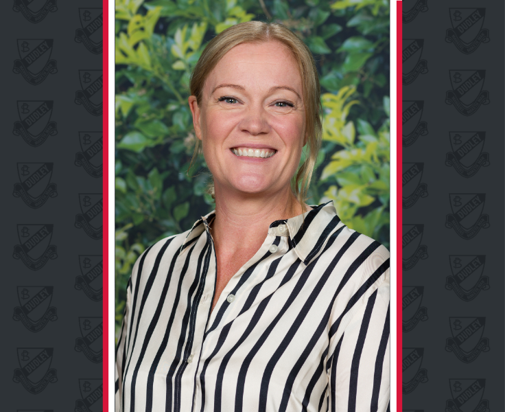 A female staff member in a vertical striped shirt smiles for the camera wit a leafy background.