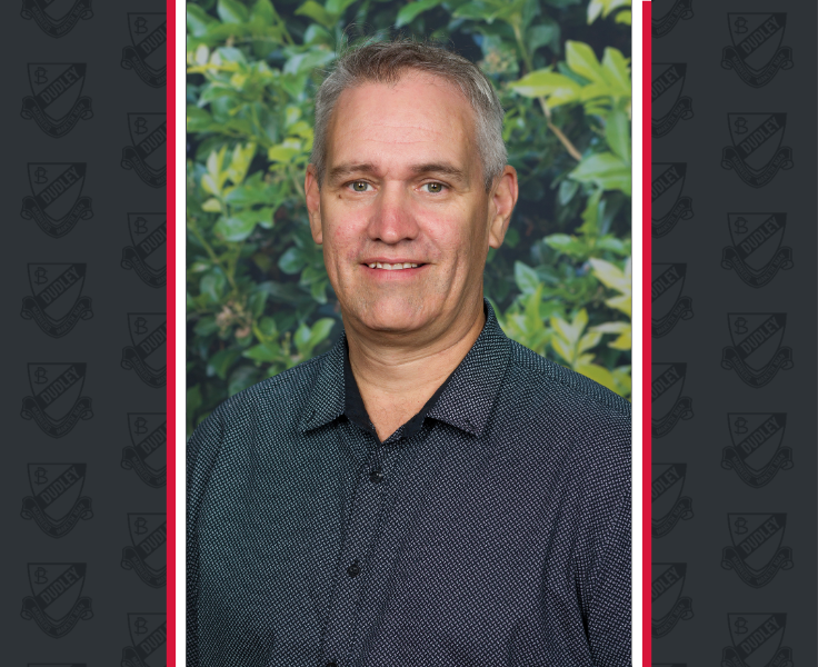 A male with a dark shirt and greying hair smailes while looking at the camera.