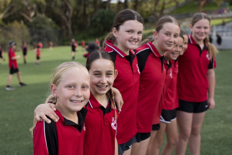 Seven girls of different ages stand in a line with their arms around each other.