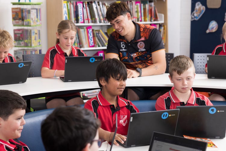 A young SLSO helps girls with her work on a Chromebook screen while three other boys do similar work in the foreground.